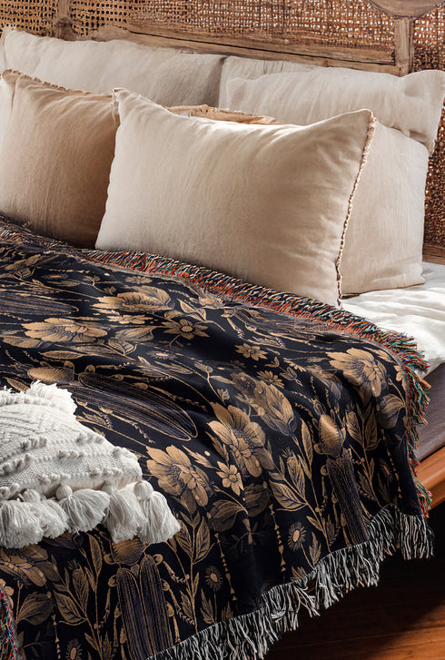 Black cotton throw blanket featuring woven bronze beetles and botanical motifs with multicolored fringe trim.